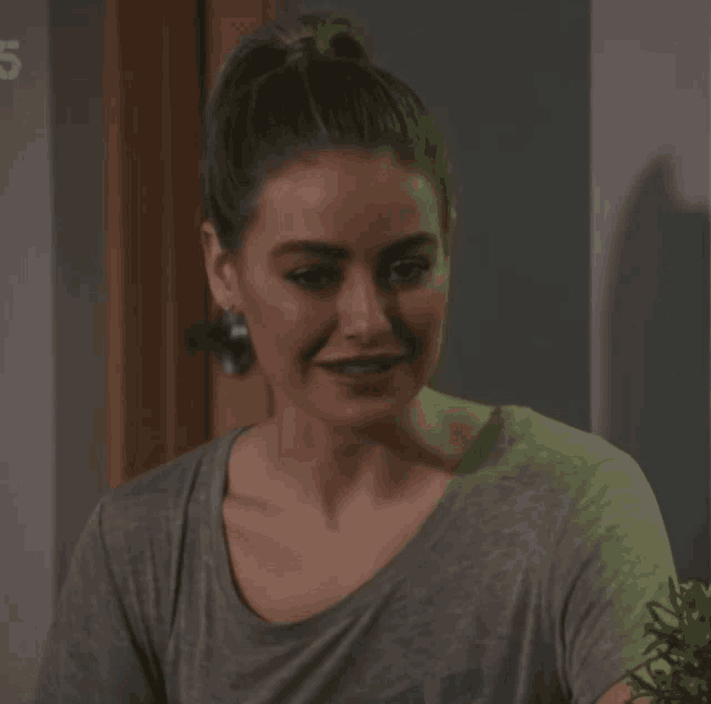 a woman in a grey shirt smiles in front of a door with the number 5 on it