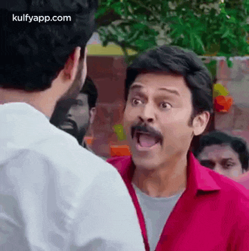 a man with a mustache is talking to another man in a red shirt .