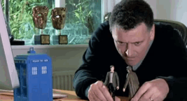 a man is sitting at a desk with a blue box that says police box on it