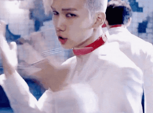 a young man wearing a white jacket and a red choker is holding a fork in his mouth .