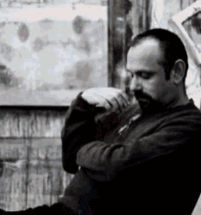 a man with a beard sits in front of a window