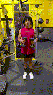 a man in a red tank top is holding two dumbbells in his hands in a gym