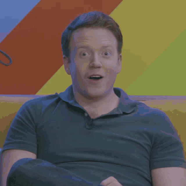 a man in a blue shirt is sitting on a yellow couch with his mouth open