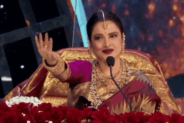 a woman in a saree is sitting in front of a microphone and waving