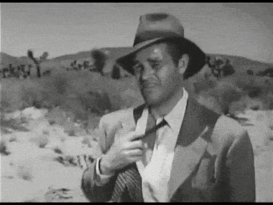 a man in a suit and hat adjusts his tie in the desert