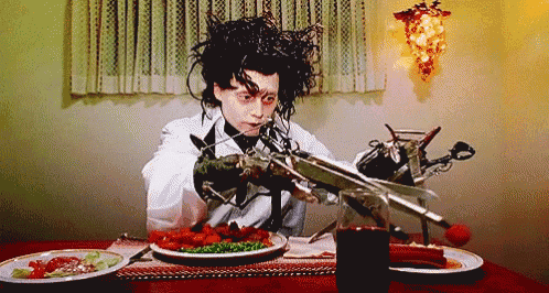 edward scissorhands is sitting at a table with plates of food