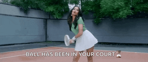 a woman in a green shirt and white skirt is playing tennis on a tennis court .