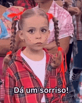 a little girl with pigtails and makeup is sitting in a crowd of people .