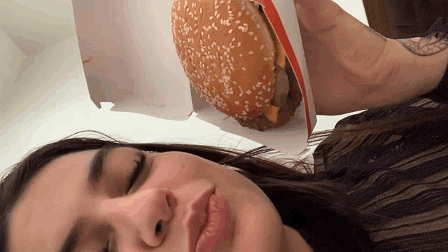 a woman is holding a hamburger with sesame seeds on the bun