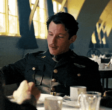 a man in a military uniform is sitting at a table eating a piece of food .