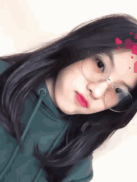 a girl wearing glasses and a green hoodie is looking at the camera