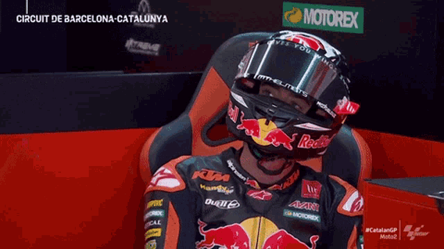 a man wearing a red bull helmet sits in a chair at circuit de barcelona catalunya
