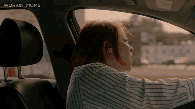 a woman in a striped shirt is driving a car with workin moms written on the bottom right