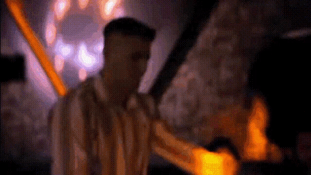 a man in a striped shirt is standing in front of a fireplace .