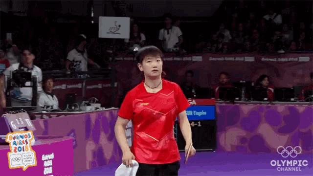 a woman in a red shirt is holding a badminton racket in front of an olympic channel banner