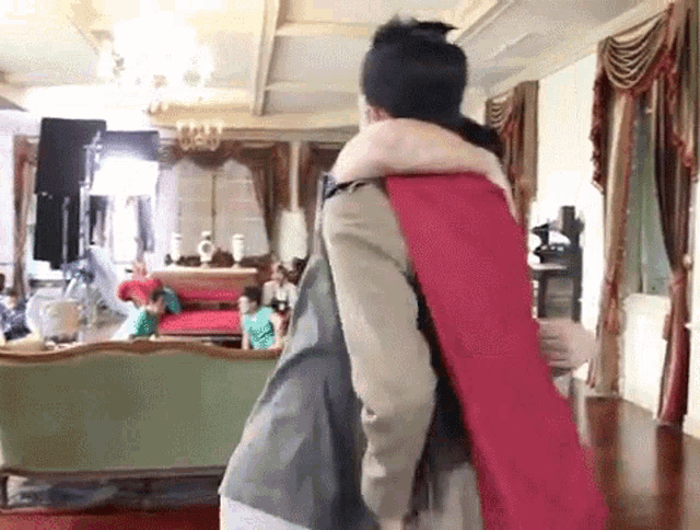 a man in a red cape is carrying another man in a living room .