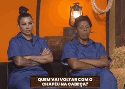 two women sitting with their arms crossed in front of a sign that says quem vai voltar como o chapeu na cabeça