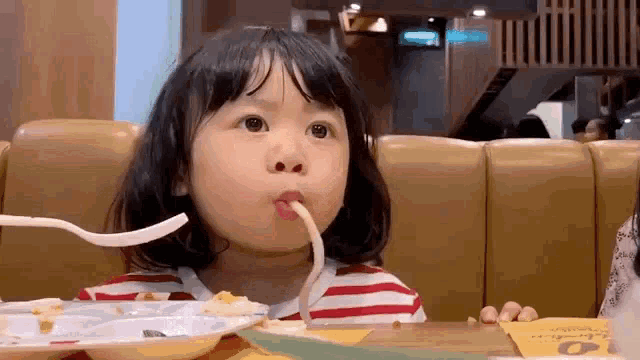 a little girl is eating spaghetti with a fork and spoon .