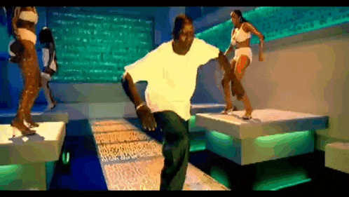 a man in a white shirt is dancing on a stage with two women in bikinis behind him