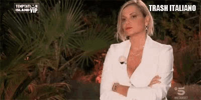 a woman in a white suit is standing with her arms crossed in front of a sign that says trash italiano .