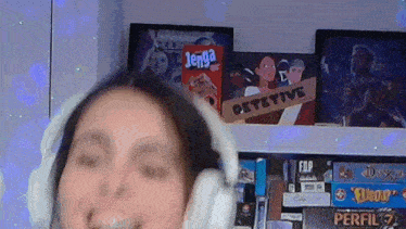 a woman wearing headphones is standing in front of a shelf full of board games including jenga and detective