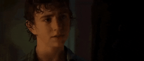 a young man with curly hair is standing in a dark room looking at the camera .