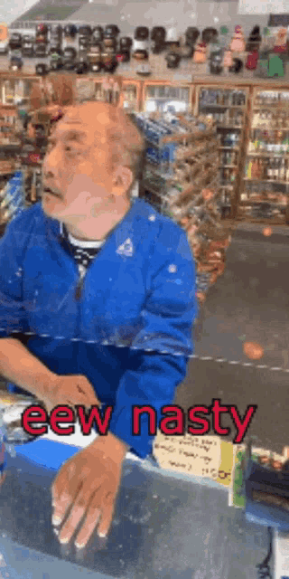 a man in a blue jacket is sitting at a counter in a store with the words eew nasty below him