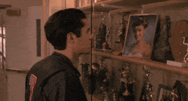 a man in a leather jacket with the number 7 on the back kisses a picture of a woman on a shelf