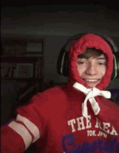 a young boy wearing a red hoodie and headphones is taking a selfie .