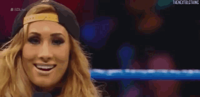 a woman wearing a hat and a microphone is smiling in a wrestling ring .