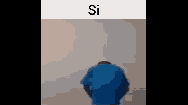 a man in a blue shirt is standing in front of a white wall with his back to the camera .