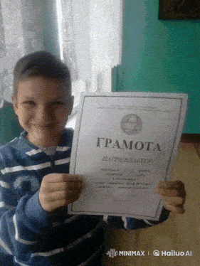 a young boy in a blue and white striped shirt holds up a certificate that says " грамота "