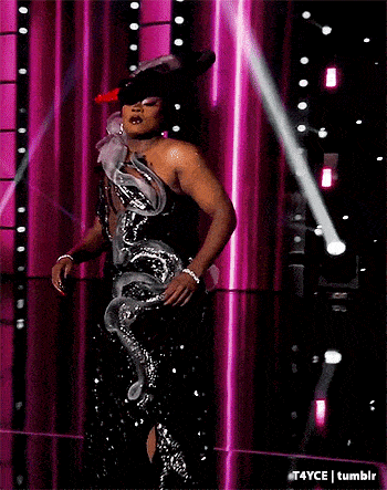 a woman is standing on a stage wearing a black and silver dress with a snake on it .