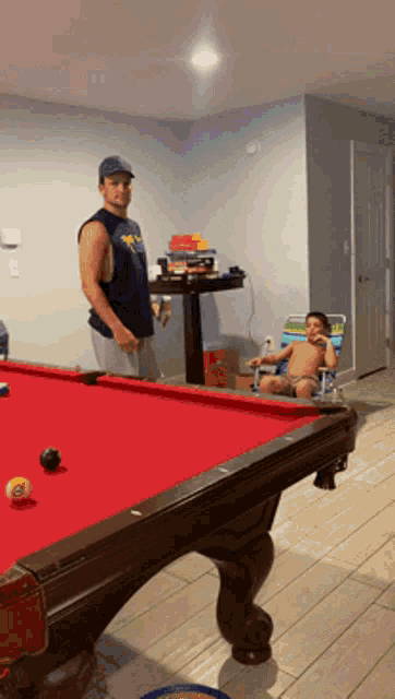 a man standing next to a pool table with a child sitting in a chair
