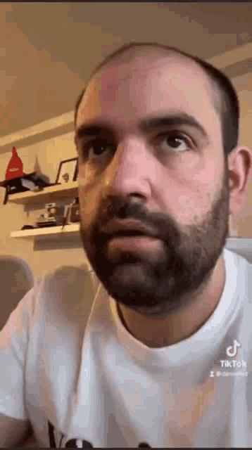a bald man with a beard is making a funny face while wearing a white shirt .