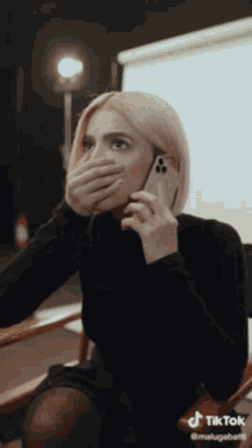 a woman covering her mouth with her hand while talking on a phone