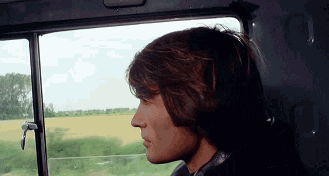 a man with long hair looks out of a window