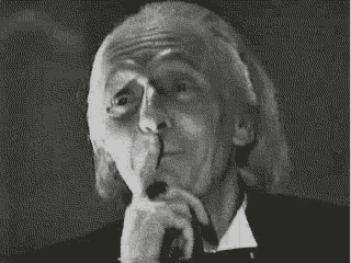 a black and white photo of an older man holding his finger to his mouth .