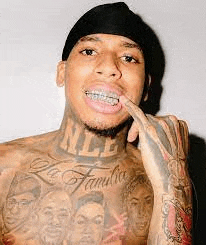 a shirtless man with braces on his teeth and a tattoo on his chest is holding his finger to his mouth .