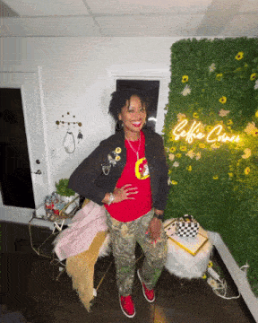 a woman stands in front of a green wall with a neon sign that says selfie goes