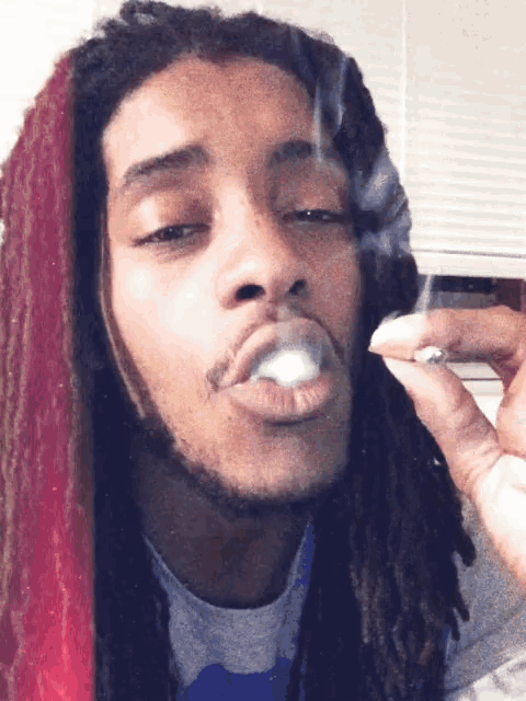 a young man with dreadlocks is smoking a cigarette