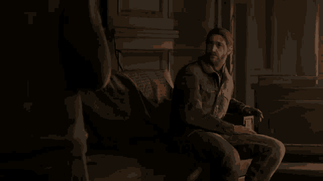 a man is sitting on a couch in a dark room talking to another man .