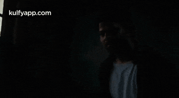 a man is standing in a dark room with a window behind him .