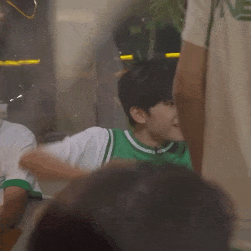 a young man in a green shirt is raising his arms in the air .