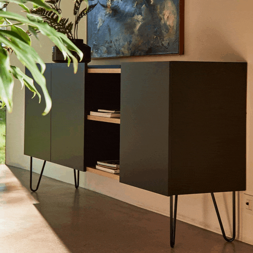 a black cabinet with hairpin legs sits next to a painting