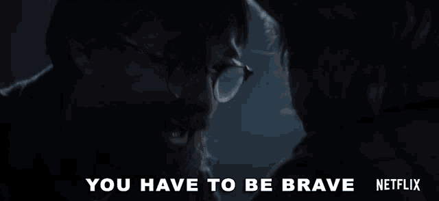 a man with glasses and a beard is talking to another man in a dark room .