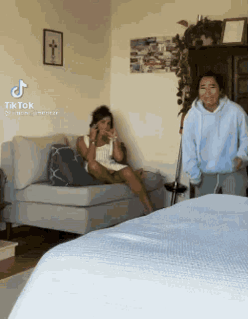 a woman is sitting on a couch in a living room while another woman stands next to her .