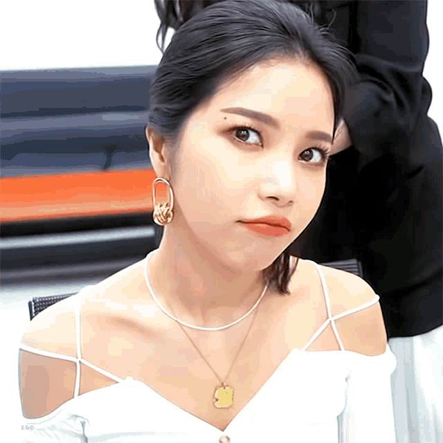 a woman wearing a white off the shoulder top and a gold necklace looks at the camera
