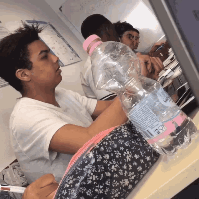 a bottle of sparkling water sits on a desk next to a boy