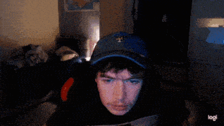 a man wearing a blue hat and a black t-shirt is sitting in front of a computer screen .